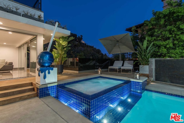 pool at twilight featuring an in ground hot tub and a patio area