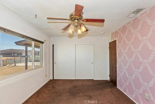 unfurnished bedroom featuring ceiling fan, a closet, dark carpet, and a textured ceiling