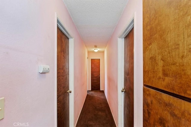 hallway featuring a textured ceiling and dark carpet