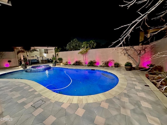 pool at night featuring an in ground hot tub and a patio area