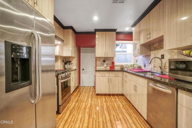 kitchen with light brown cabinetry, backsplash, appliances with stainless steel finishes, dark stone countertops, and sink