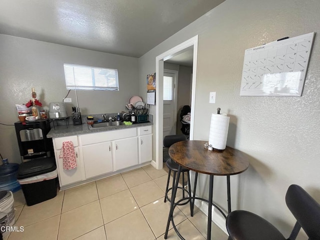 kitchen with sink, a textured ceiling, white cabinets, and light tile patterned flooring