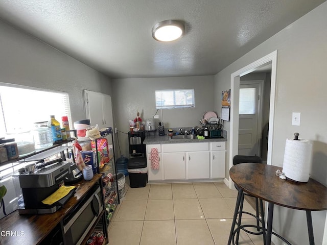 kitchen with white cabinets, sink, light tile patterned floors, and a textured ceiling