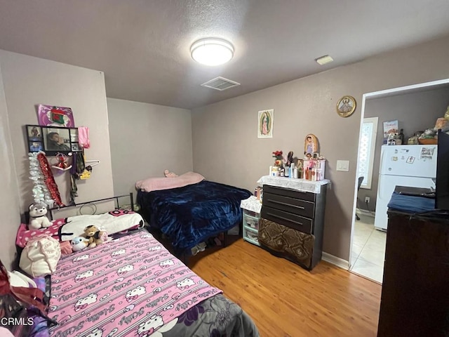 bedroom featuring white refrigerator, a textured ceiling, and light hardwood / wood-style flooring