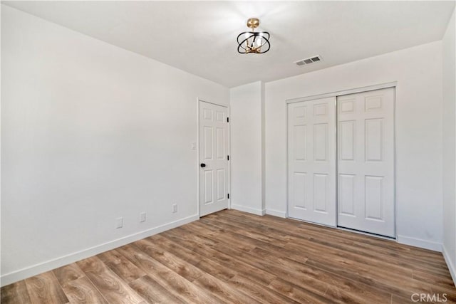 unfurnished bedroom with wood finished floors, visible vents, a closet, and baseboards