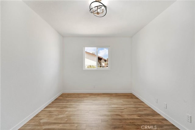 empty room featuring wood finished floors, baseboards, and a chandelier