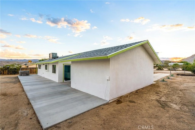 rear view of house with stucco siding, roof with shingles, central AC, and fence