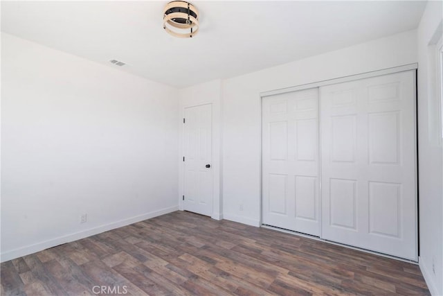 unfurnished bedroom with a closet, visible vents, baseboards, and wood finished floors