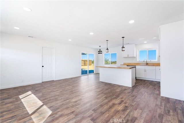 kitchen with wood finished floors, a kitchen island, a healthy amount of sunlight, and white cabinets