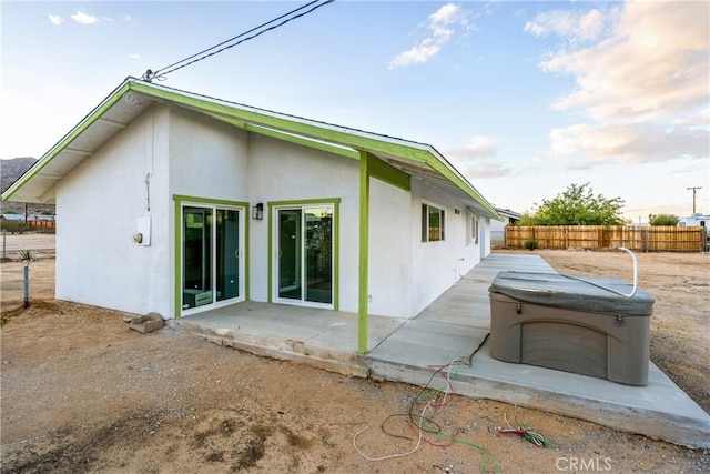 rear view of property featuring a patio, fence, a hot tub, and stucco siding