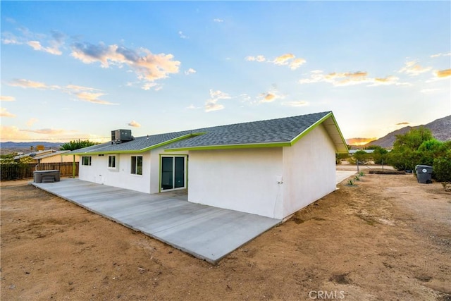 rear view of property featuring stucco siding, roof with shingles, central AC, and fence