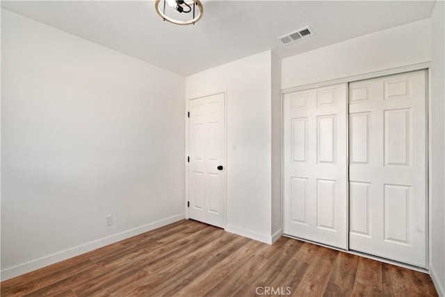 unfurnished bedroom featuring a closet, visible vents, baseboards, and wood finished floors