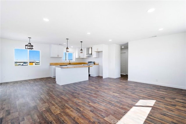 kitchen featuring white cabinetry, wall chimney range hood, open floor plan, and a kitchen island