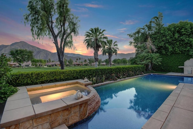 pool at dusk featuring a mountain view and an in ground hot tub