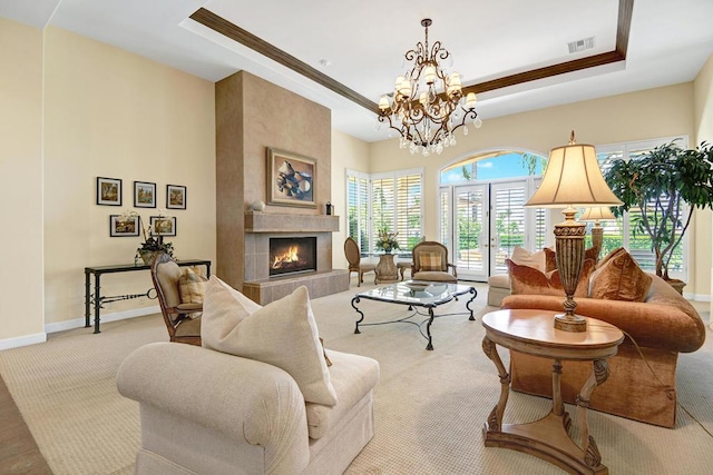 living room with light colored carpet, a notable chandelier, a tile fireplace, and a tray ceiling