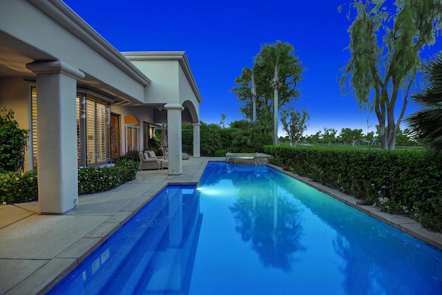 pool at dusk featuring an in ground hot tub and a patio