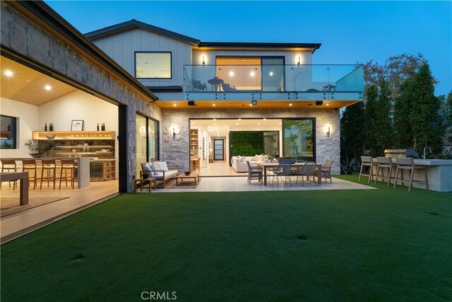 rear view of property featuring an outdoor bar, a balcony, and a yard