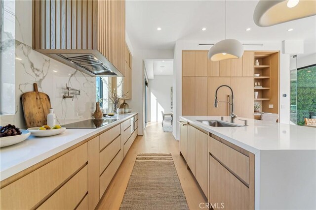 kitchen with black electric stovetop, light brown cabinetry, a center island with sink, and sink