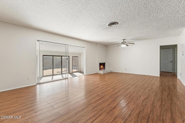 unfurnished living room with a textured ceiling, ceiling fan, light wood-type flooring, and a fireplace