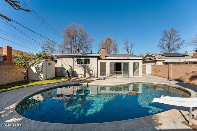 back of property featuring a patio area, a storage unit, cooling unit, and a fenced in pool