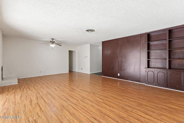 unfurnished living room featuring a textured ceiling, ceiling fan, light hardwood / wood-style floors, and a brick fireplace