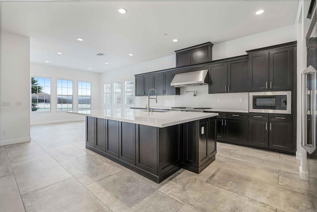 kitchen with sink, wall chimney range hood, a kitchen island with sink, and built in microwave