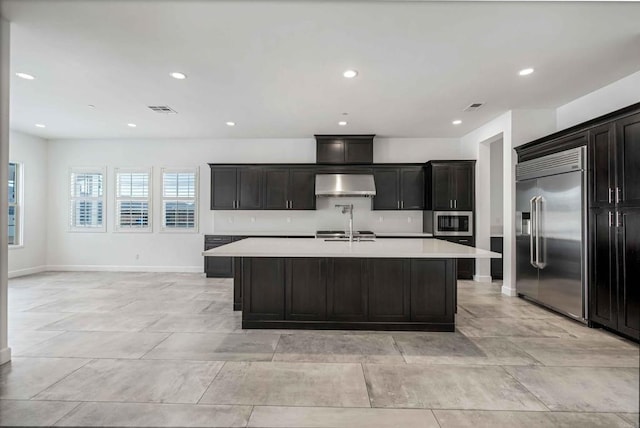 kitchen with appliances with stainless steel finishes, wall chimney range hood, a kitchen island with sink, and sink