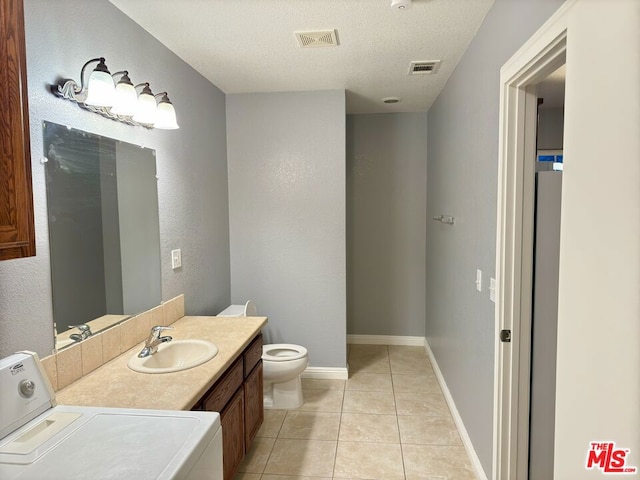 bathroom featuring a textured ceiling, washer / clothes dryer, tile patterned floors, vanity, and toilet