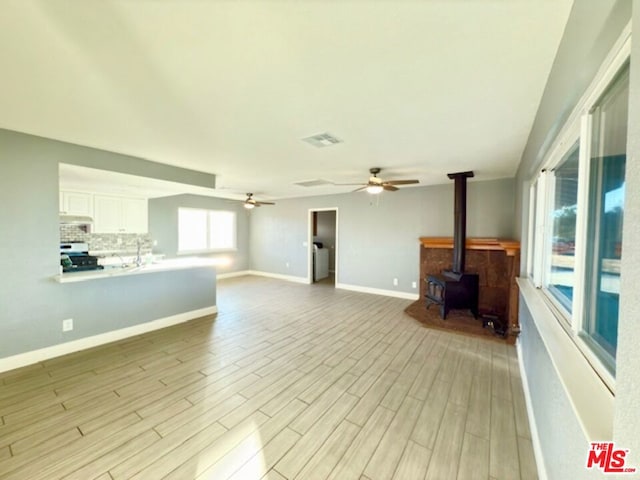 unfurnished living room featuring ceiling fan, a wood stove, and light hardwood / wood-style flooring