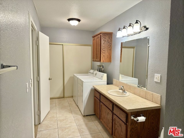 clothes washing area with washing machine and dryer, light tile patterned floors, a textured ceiling, and sink