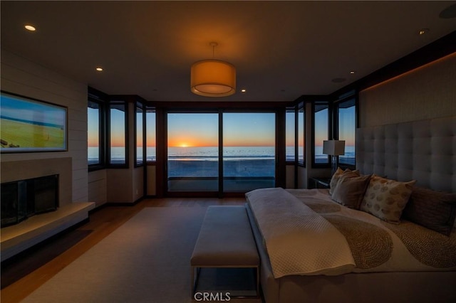 bedroom featuring recessed lighting, a water view, wood finished floors, access to exterior, and a glass covered fireplace