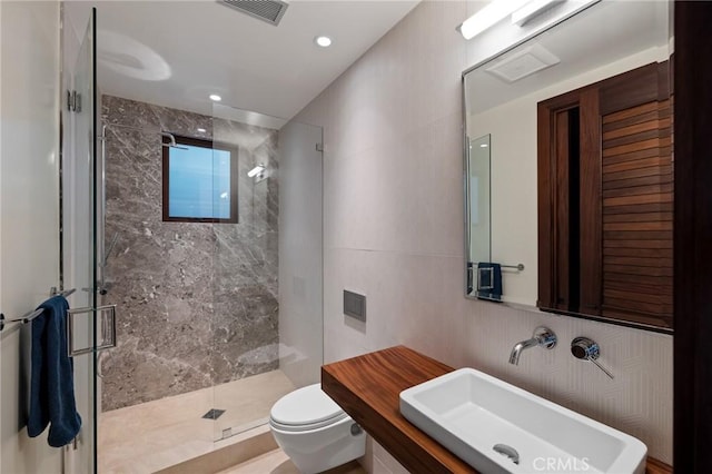 bathroom with toilet, a sink, visible vents, tile walls, and a stall shower