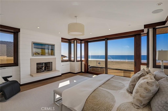 bedroom featuring access to exterior, a beach view, a water view, a glass covered fireplace, and wood finished floors