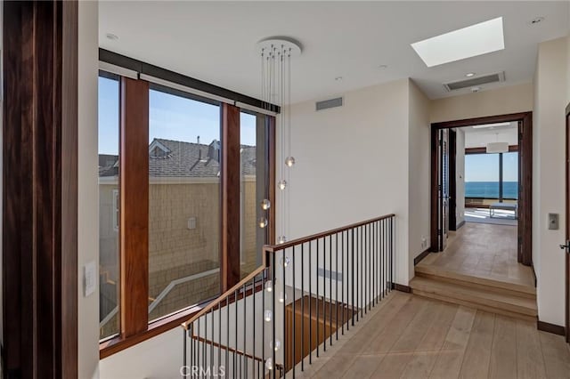 hallway featuring a skylight, visible vents, wood finished floors, and an upstairs landing