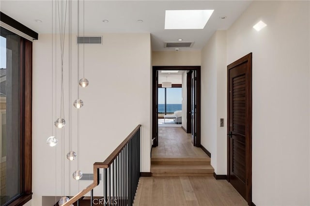 hallway with light wood-type flooring, visible vents, baseboards, and a skylight