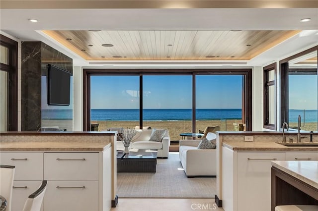 kitchen with wooden ceiling, white cabinetry, a sink, and a water view