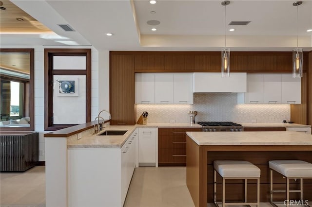 kitchen with visible vents, decorative backsplash, a peninsula, a kitchen bar, and a sink