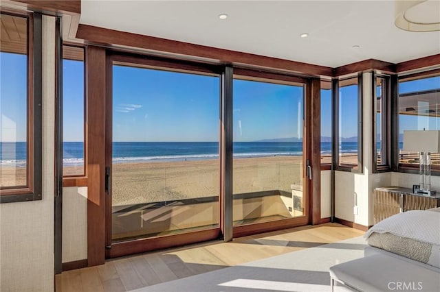 unfurnished bedroom featuring a view of the beach, multiple windows, a water view, and wood finished floors