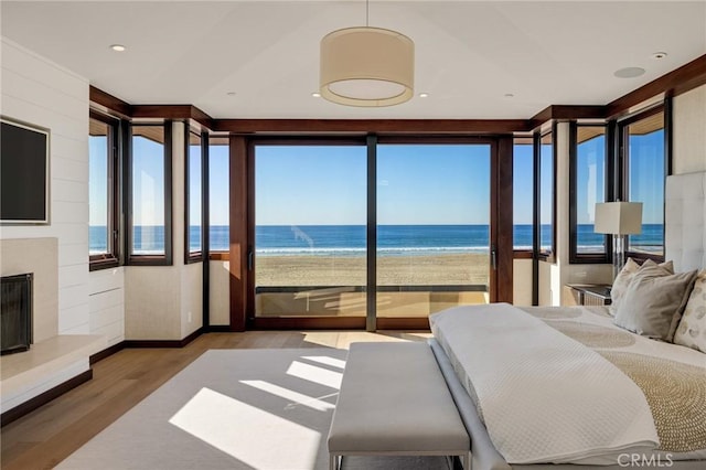 bedroom with a fireplace with raised hearth, a view of the beach, a water view, wood finished floors, and access to outside