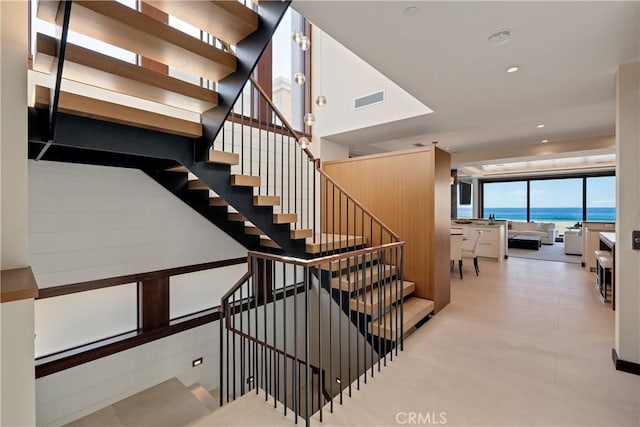 staircase featuring recessed lighting, visible vents, and a water view