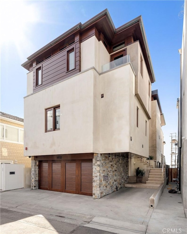 exterior space featuring stucco siding, concrete driveway, a balcony, a garage, and stone siding