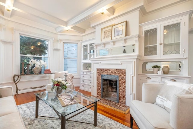 living area featuring beamed ceiling, light hardwood / wood-style flooring, a premium fireplace, coffered ceiling, and baseboard heating