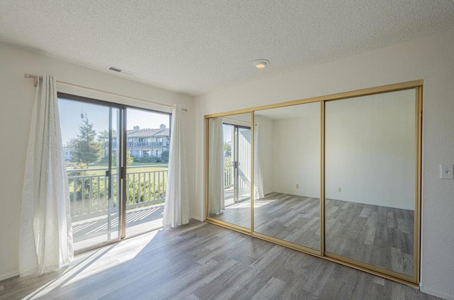 unfurnished bedroom with a textured ceiling, light hardwood / wood-style floors, access to exterior, and a closet