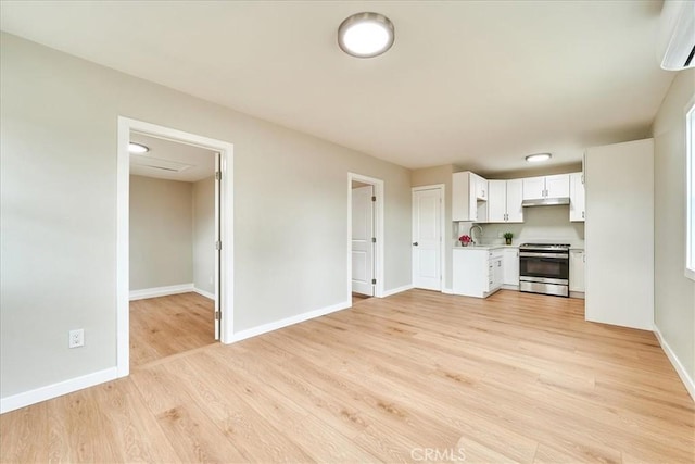 kitchen with sink, stainless steel stove, white cabinetry, light hardwood / wood-style floors, and an AC wall unit