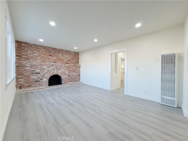 unfurnished living room with a brick fireplace, brick wall, and light hardwood / wood-style floors