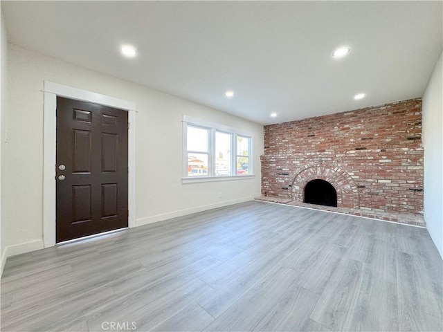 unfurnished living room featuring a brick fireplace, brick wall, and light wood-type flooring