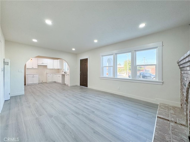 unfurnished living room with a fireplace, sink, and light wood-type flooring