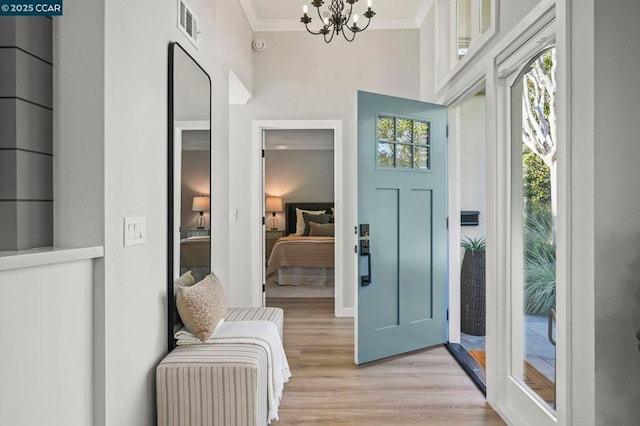 foyer entrance featuring light wood-type flooring, a notable chandelier, and ornamental molding