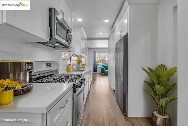 kitchen with sink, white cabinetry, light hardwood / wood-style flooring, and appliances with stainless steel finishes