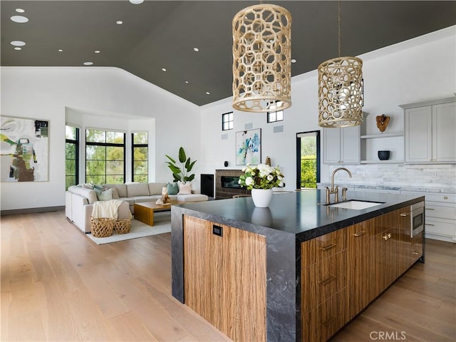 kitchen with sink, white cabinets, light hardwood / wood-style floors, backsplash, and a center island with sink